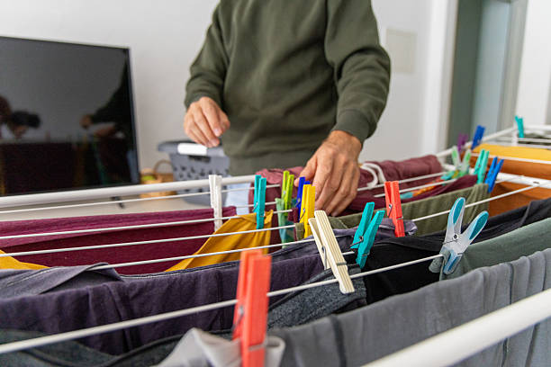 Man arranging laundry on drying rack in living room. Household chore of drying clothes indoors. Domestic scene of managing home tasks.