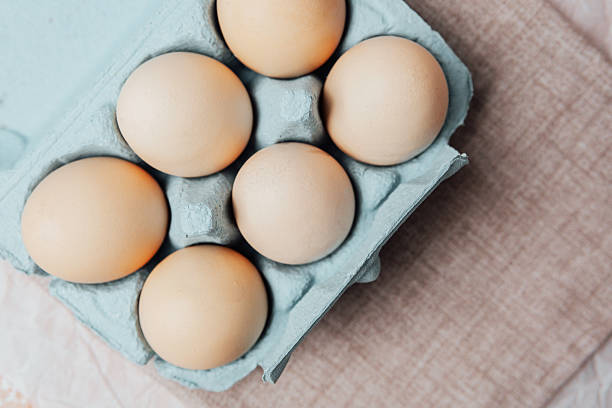 istock Brown chicken eggs in a blue carton box on light blue background, top view 2211907491