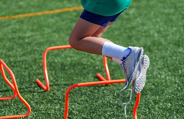 istock Young athlete jumping over orange mini hurdles on turf field 2211910510