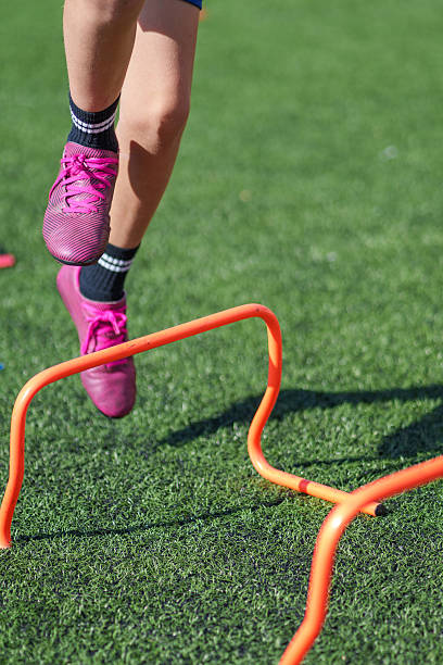 istock Young athlete jumping over orange hurdle on turf field during training 2211910901