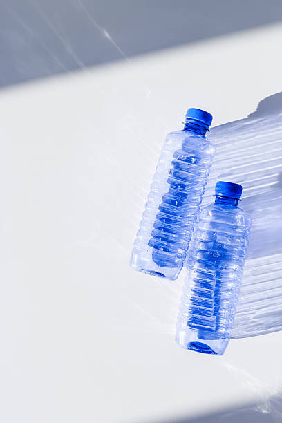 istock Clear plastic water bottles for clean water on white blue background closeup, minimal aesthetic lifestyle photo, top view, flat lay, Naural light, sunlight shadows, caustic light effect, star filter 2211911083
