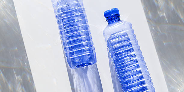 istock Blue plastic water bottles on white blue background with sunlight shadow and sun flare, Minimal top view banner, themes of ecology, recycling, sustainable living, reduce disposable plastics 2211911084