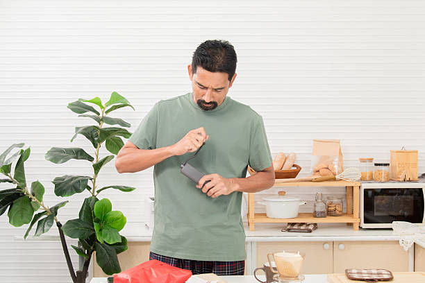 istock Middle-aged bearded Asian man grinds coffee beans with traditional coffee grinder using hand-crank to make the coffee beans powdered for drink in morning at home. Healthy lifestyle concept. 2211911587