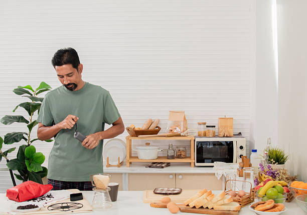 istock Middle-aged bearded Asian man grinds coffee beans with traditional coffee grinder using hand-crank to make the coffee beans powdered for drink in morning at home. Healthy lifestyle concept. 2211911601