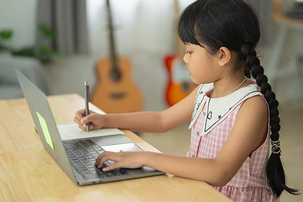 istock Young girl engaged in home study session, writing notes while using laptop, bright and cozy indoor environment, learning and creativity concept 2211911823