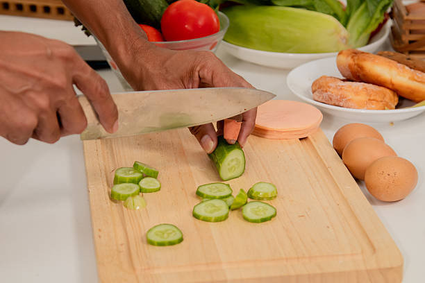 Asian man with beard sitting makes sandwich and divide two peice with knife in kitchen for breakfast in morning. Male wear apron enjoy make food for health care in house, healthy food at home.