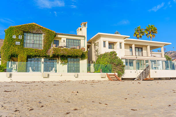 Malibu, California - December 21, 2024: Picturesque view of luxurious beachfront homes in showcasing modern architecture and lush greenery against a vibrant blue sky.
