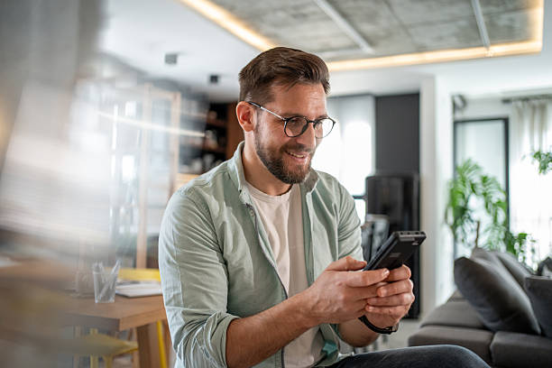 istock Smiling young man using smartphone at home in living room 2211915866