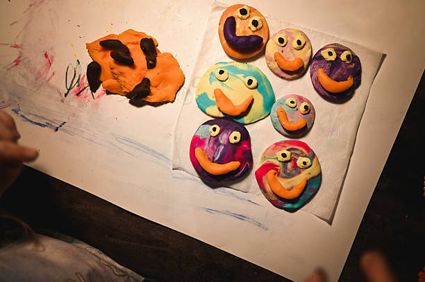 Kids playing with colorful modeling clay, creating funny smiley faces on a white sheet of paper