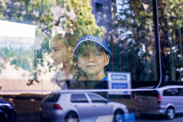 View from the street through bus glass, showing reflective faces of two children. Themes of observation, urban travel, emotion, and childhood awareness.