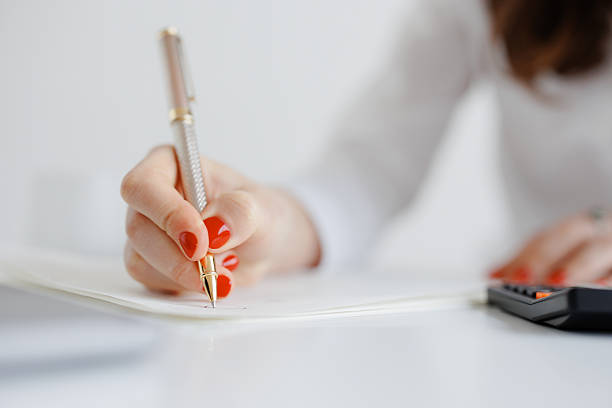istock Woman writing notes with a pen and calculator on a desk during a work session in a bright, minimalist office space 2211918549