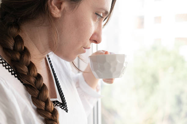 Woman drinking cup of tea at window