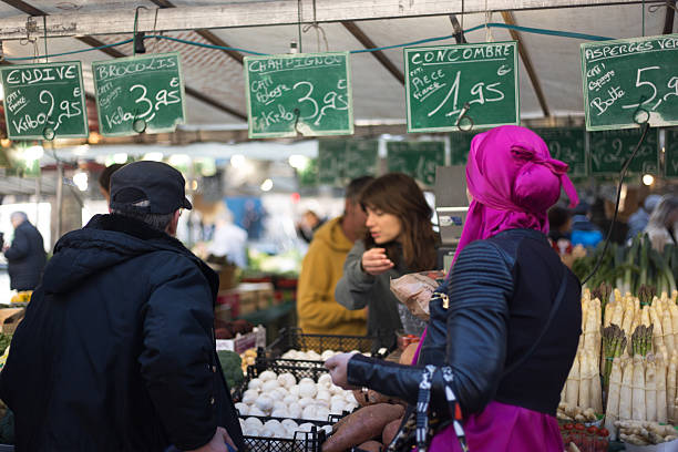 Paris, France: An elegant shopper in a vibrant purple headscarf shops at a veggie stall in the bi-weekly Bastille market, 11th arrondissement.