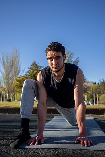 istock Athletic man stretching on exercise mat in park during sunny day, preparing for workout with focus and balance in low lunge position 2211923288