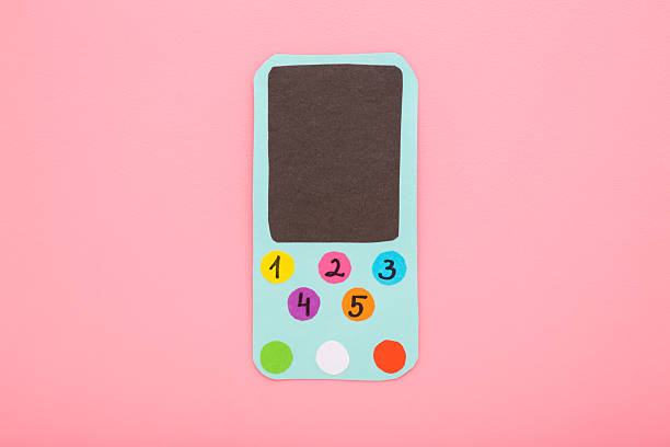 Smartphone made from colorful application paper on light pink table background. Pastel color. Creating child gadget for playing. Closeup. Top down view.