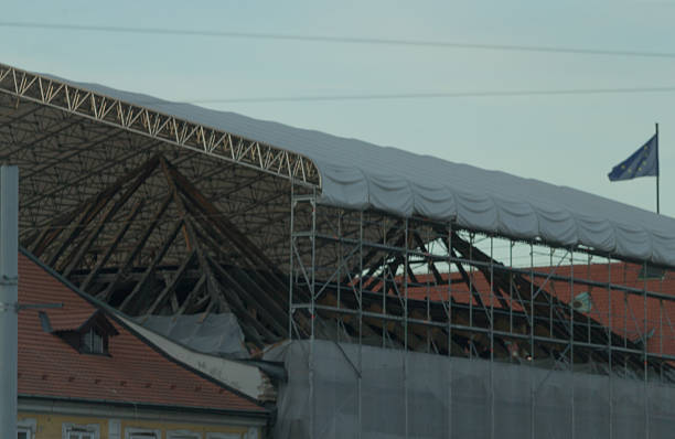 A damaged roof structure under construction is nearby a displayed flag