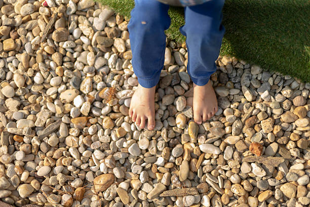A barefoot child happily standing on a collection of pebbles in a lush garden area, fully engaged in exploration and play