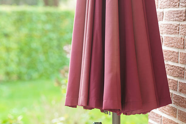 Closed red patio umbrella in front of a brick wall in garden setting
