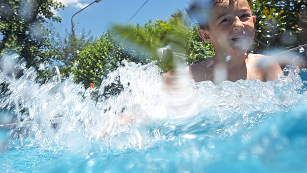 Child playing, swimming and splashing in the swimming pool in the backyard at home on a sunny day. Summer vacations and water fun.