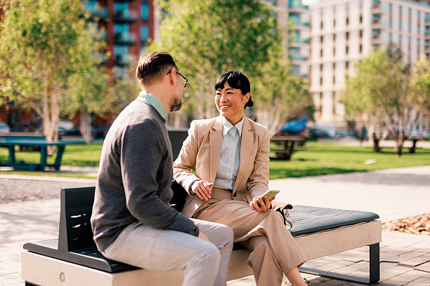 istock Business partners discussing a project sitting on a bench in a park 2211946182