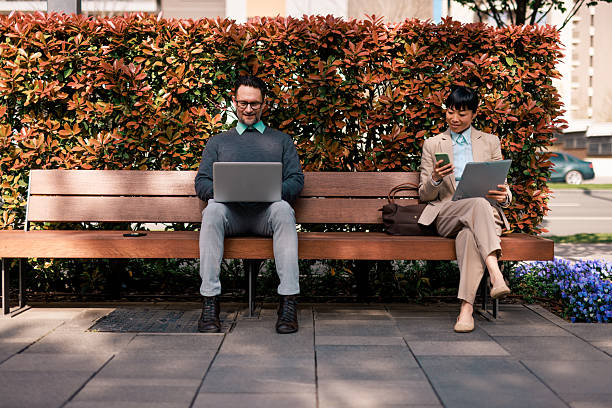 istock Business people working outdoors with laptop and smartphone sitting on bench 2211946426