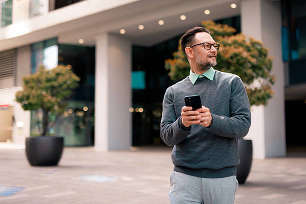 istock Smiling businessman using smartphone and walking near office building 2211947177