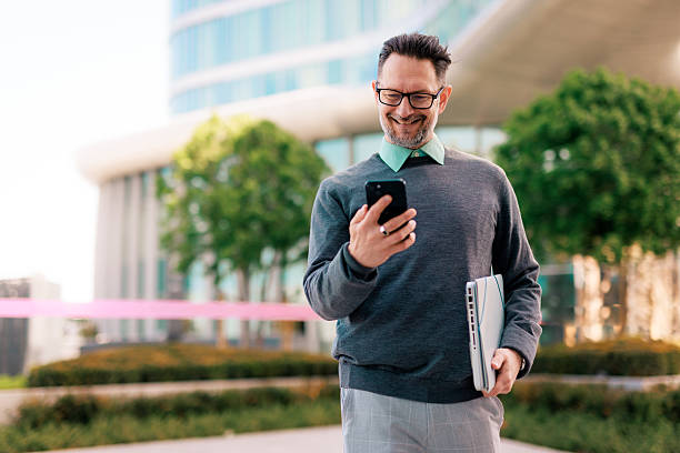 istock Smiling businessman using smartphone and carrying laptop in urban setting 2211949006