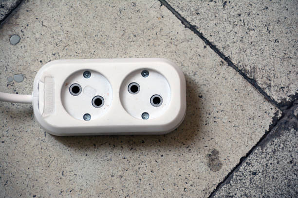 White power plug on the floor. Electric power socket and electrical wire on the brick wall background. Power plug on the floor