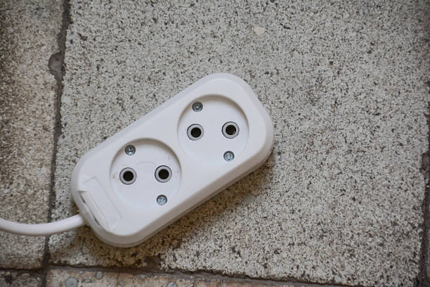White power plug on the floor. Electric power socket and electrical wire on the brick wall background. Power plug on the floor