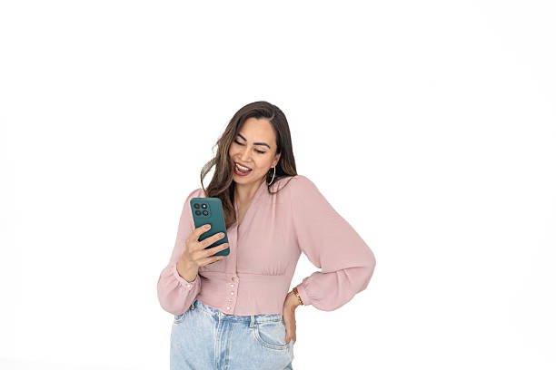 istock Young woman interacts with mobile app on her phone while smiling against a bright white background 2211956589