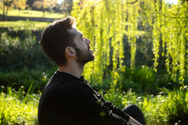 istock A smiling man with a beard stands outdoors under bright sunlight, surrounded by lush green trees. He is wearing a black shirt and looks happy and relaxed in the natural setting. 2211959545