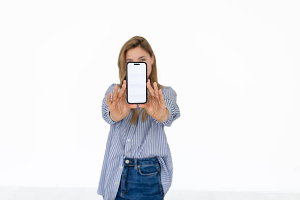 A young woman interacts with an application on her smartphone, displaying happiness as she holds the device in front of her against a clean white background.
