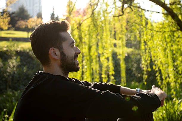 istock A smiling man with a beard stands outdoors under bright sunlight, surrounded by lush green trees. He is wearing a black shirt and looks happy and relaxed in the natural setting. 2211960278