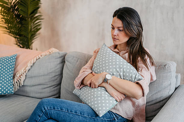 istock Sad Young Woman Embracing A Pillow While Sitting At Home On The Sofa 2211960371