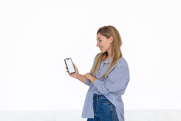 A young woman is smiling and engaged while using her smartphone to interact with a mobile application. The contrasting white background highlights her enthusiasm and connection to technology.