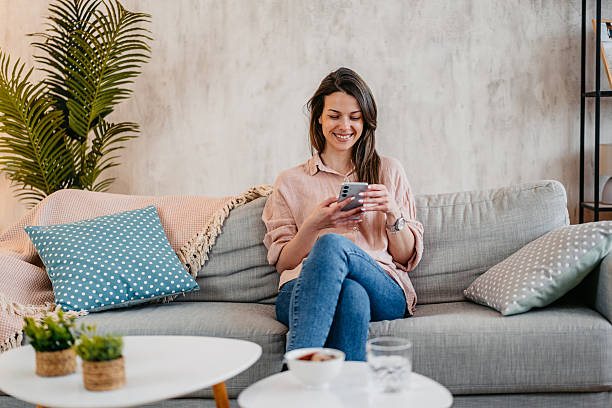 istock Young Woman Texting On The Phone While Sitting On The Sofa At Home 2211960715