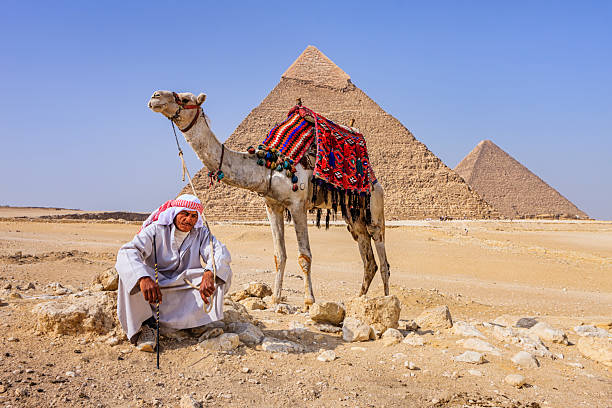 Giza, Cairo, Egypt. February 18, 2022. Man on a camel with deocrated blanket and halter at the Great Pyramid complex in Giza.