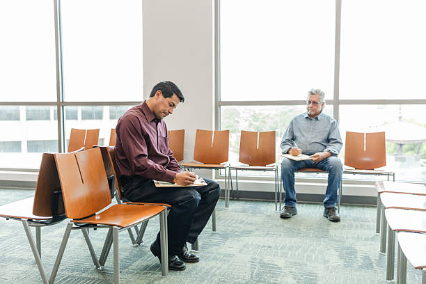 istock Two Men Sitting in a Waiting Room, Filling Out Forms 2211963520