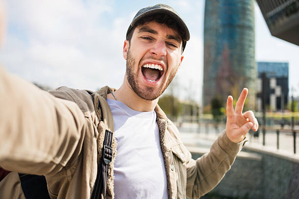 istock Young man student with backpack and cap taking selfie photo with mobile phone in Barcelona 2211966548