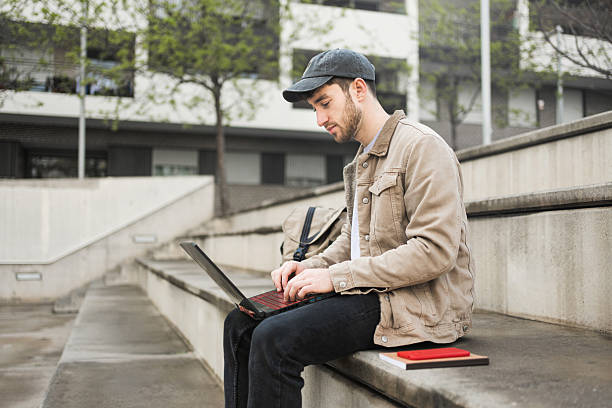 istock College male student working on laptop sitting on university campus steps 2211966719