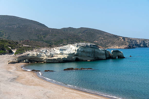 White volcanic rock formations rise above the calm, clear waters of Triades Beach, a hidden gem on the remote western coast of Milos, Greece. Known for its raw natural beauty and tranquil atmosphere, the beach features unique geological formations shaped by volcanic activity.
