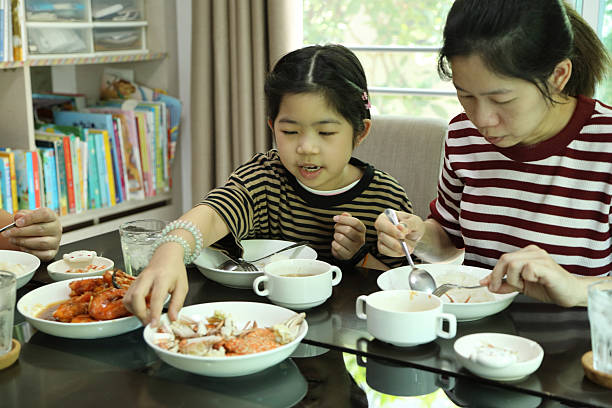 An East Asian girl is having lunch with her parents in the dining room.