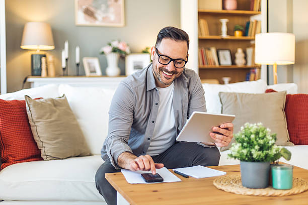 istock Smiling man managing domestic finances with tablet and smartphone on sofa 2211984475