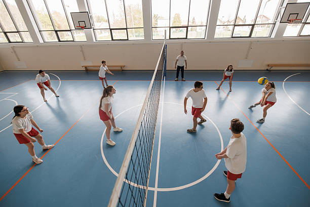 Group of teenage children are playing a volleyball game in school gym