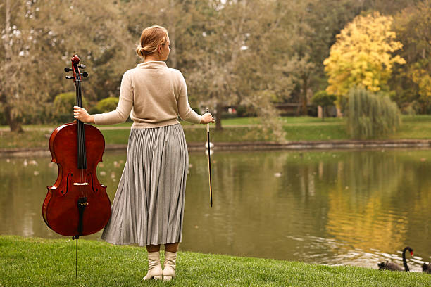 Young woman with cello in park, back view. Space for text