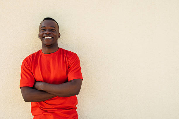 istock Smiling Man in a Red Shirt Standing Against a Plain Beige Wall 2211990418