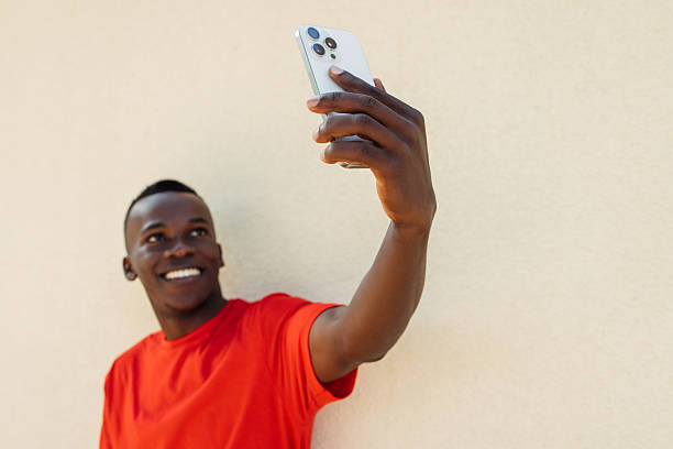 istock Young man capturing a selfie while happily posing against a beige wall 2211990474