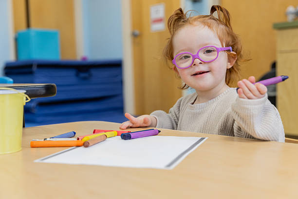 istock Creative Toddler With Down Syndrome Drawing at Desk 2211991550