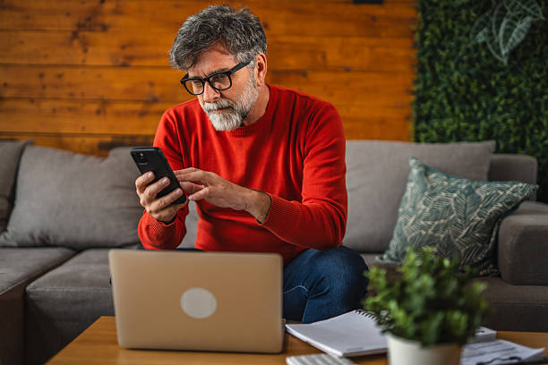 istock Modern senior man sit on sofa with laptop and use mobile phone 2212006949