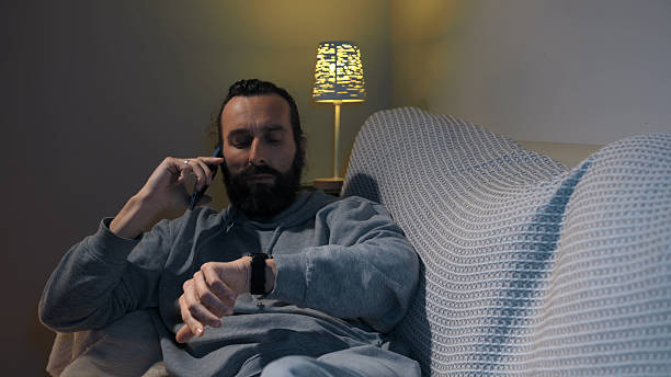 istock Relaxed Man at Home on Phone and Checking Watch in Cozy Setting 2212007012